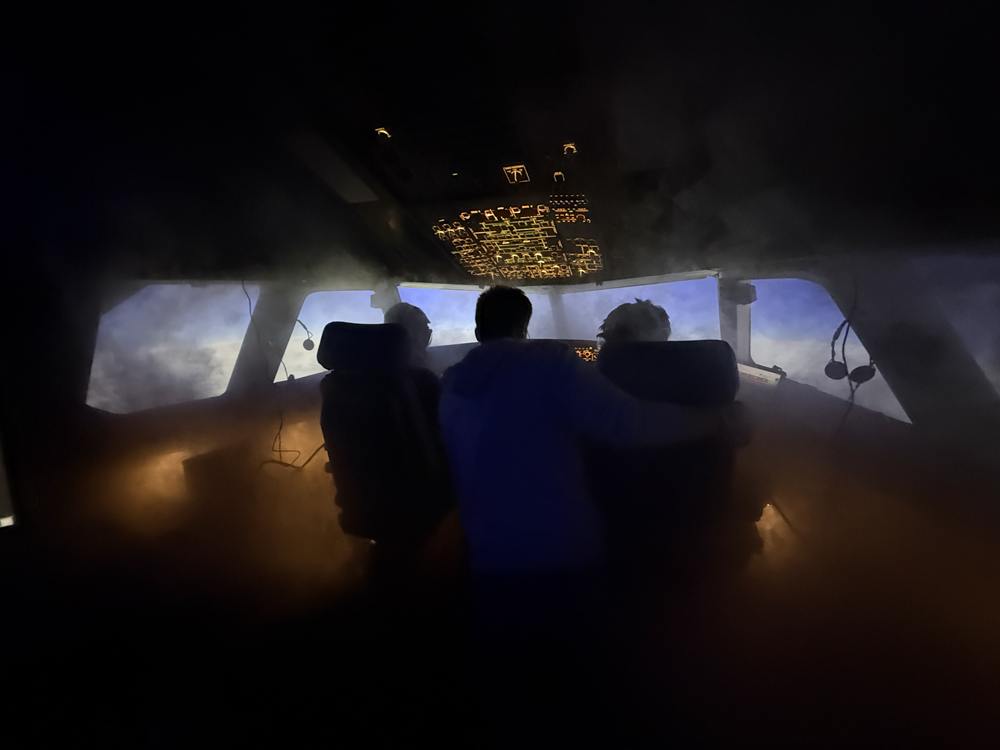 Drei Teilnehmer gemeinsam im Cockpit, einer legt den Arm um die beiden Piloten