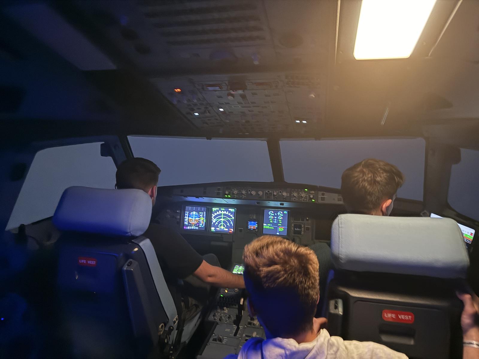 Zwei Personen auf den Pilotensitzen im Airbus-Simulator, eine dritte verfolgt den Flug vom Jumpseat direkt dahinter